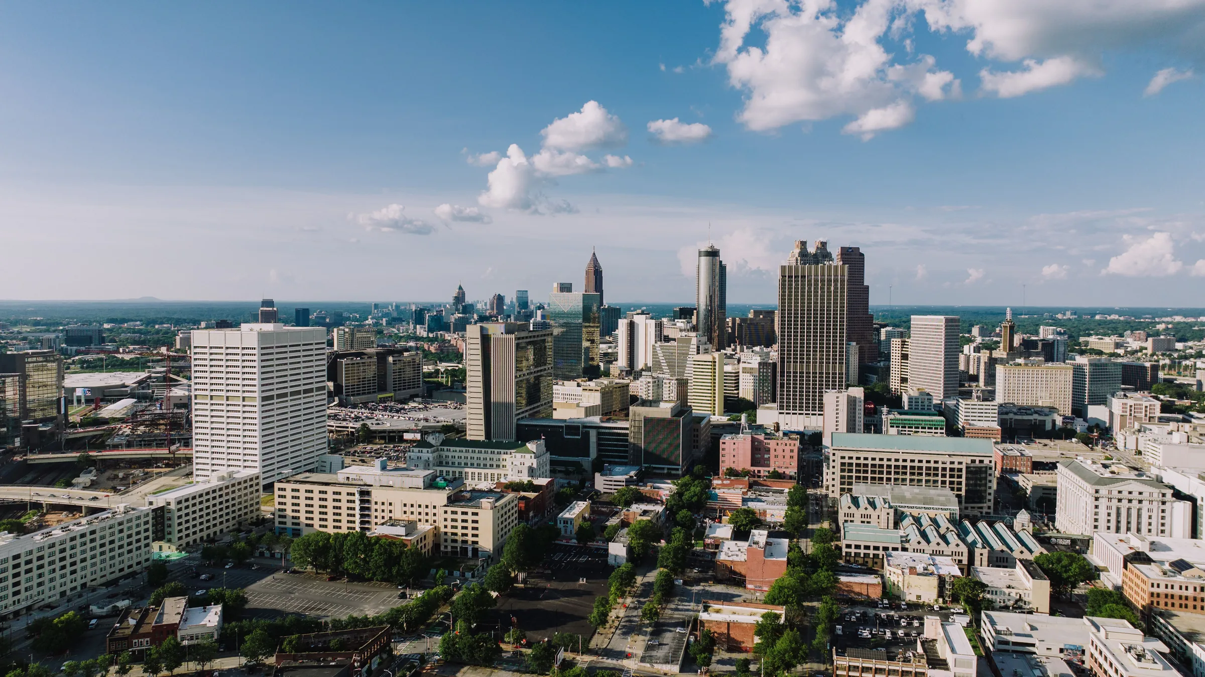 Aerial view of Atlanta's downtown skyline with tall buildings and blue sky with white clouds.