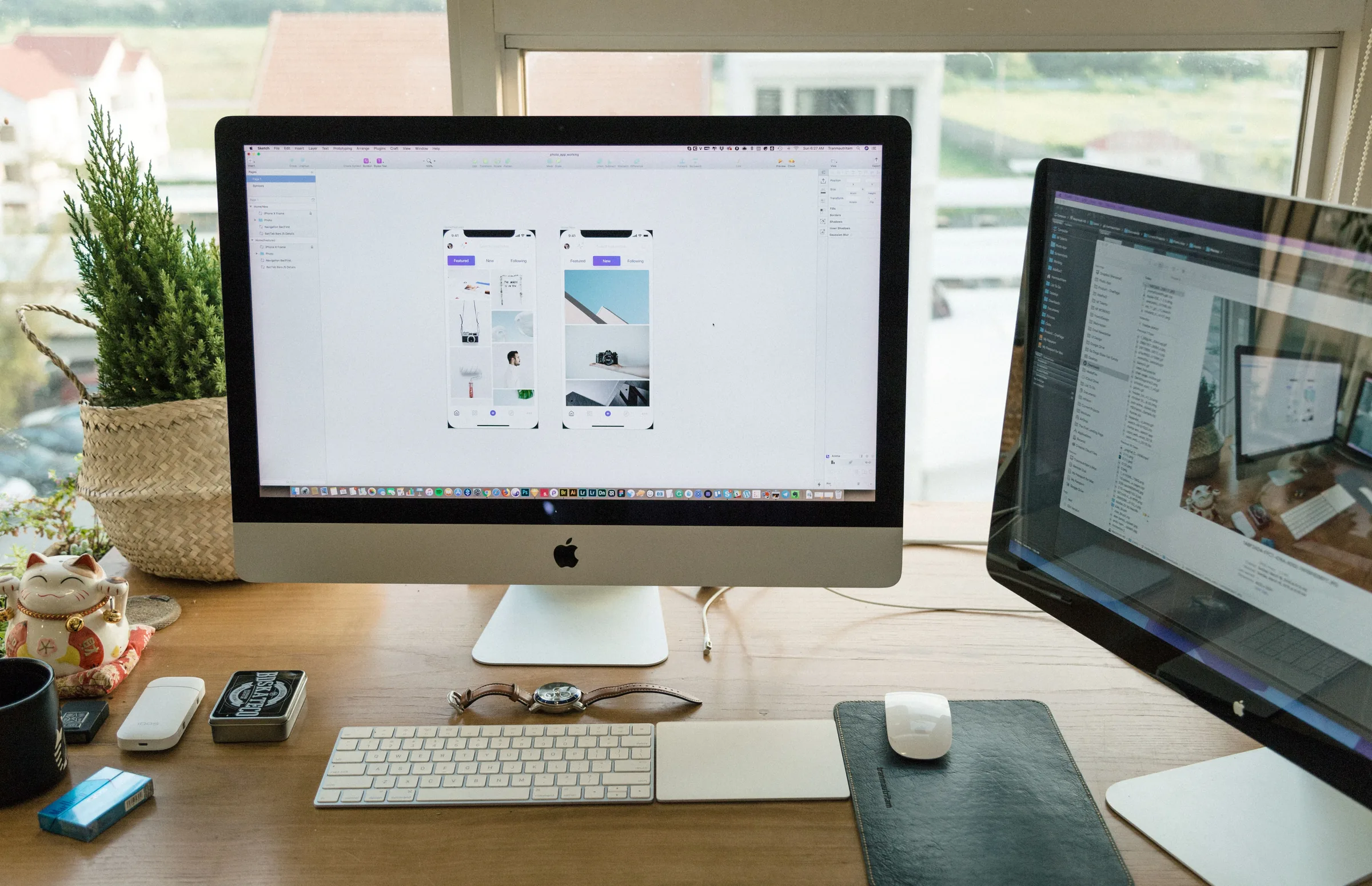 Designer workspace with iMac displaying mobile app mockups, second monitor, keyboard, mouse, and desk plants.
