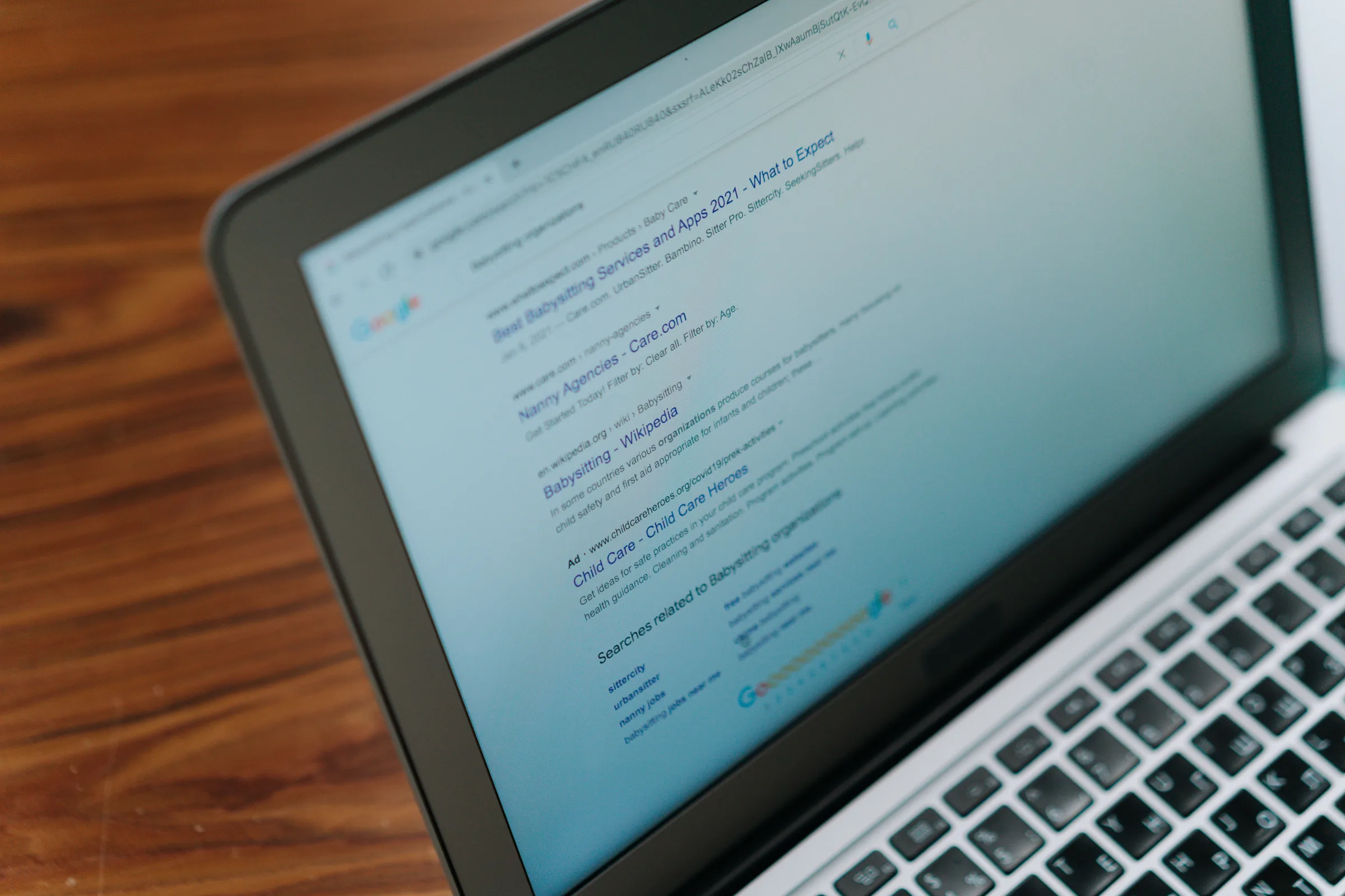 Laptop displaying Google search results for babysitting services and childcare agencies.