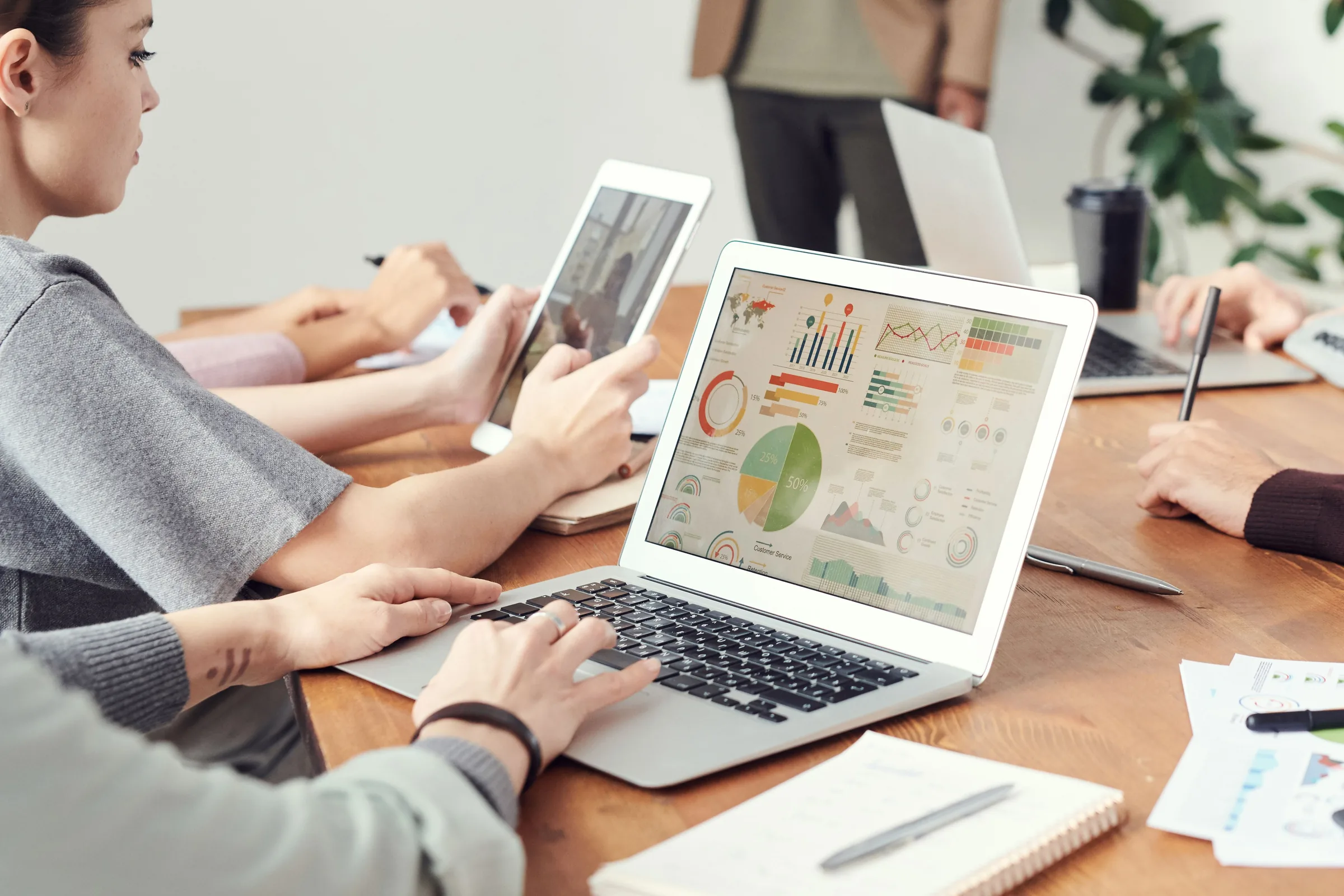 Team members review data analytics and charts on laptop and tablet during business meeting.